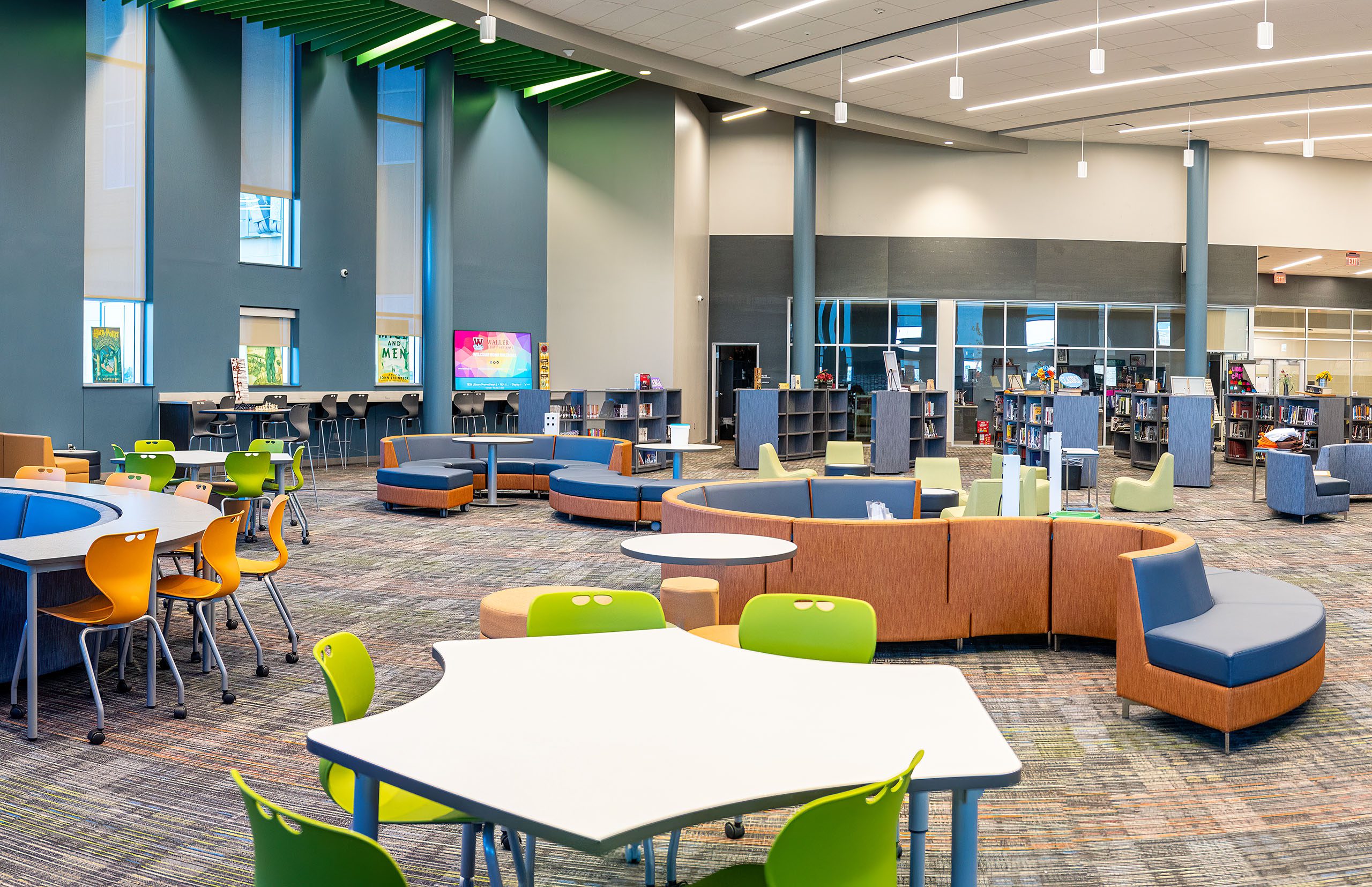 Spacious modern school library with colorful, flexible seating including curved blue and orange sofas and bright green chairs.